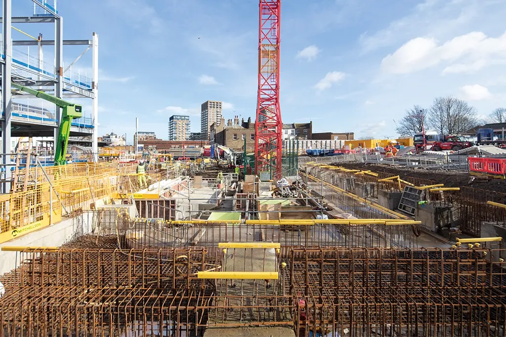 Construction site with steel reinforcement, concrete foundations, workers and a tower crane.
